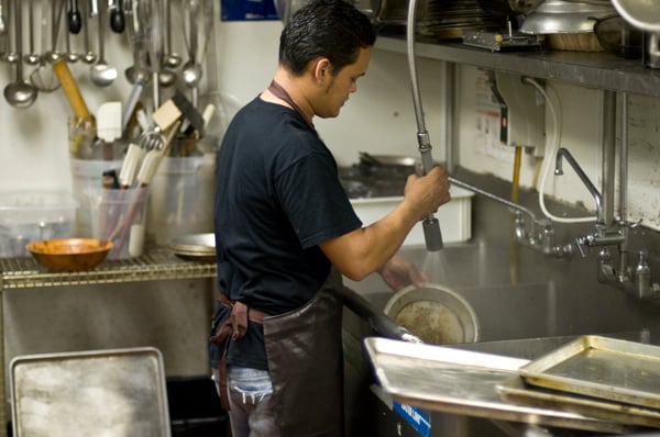 Man rinsing dishes in restaurant kitchen